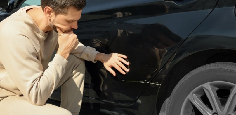 Uomo esamina con preoccupazione un graffio sulla carrozzeria dell'auto, tipico esempio di danni da parcheggio.