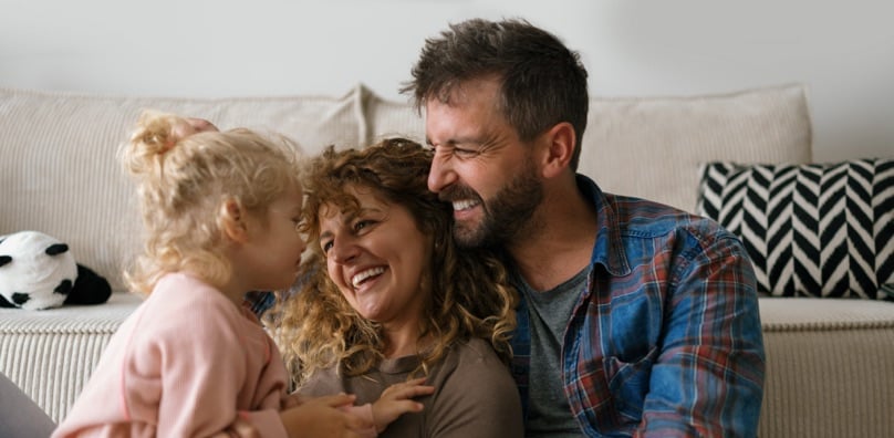 Famiglia felice in soggiorno che sorride, simbolo di serenità e assicurazioni per un futuro sicuro.