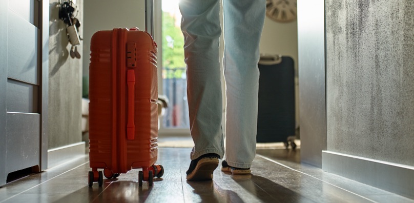 Persona esce di casa con una valigia prima di un viaggio, situazione a rischio per i furti in vacanza.