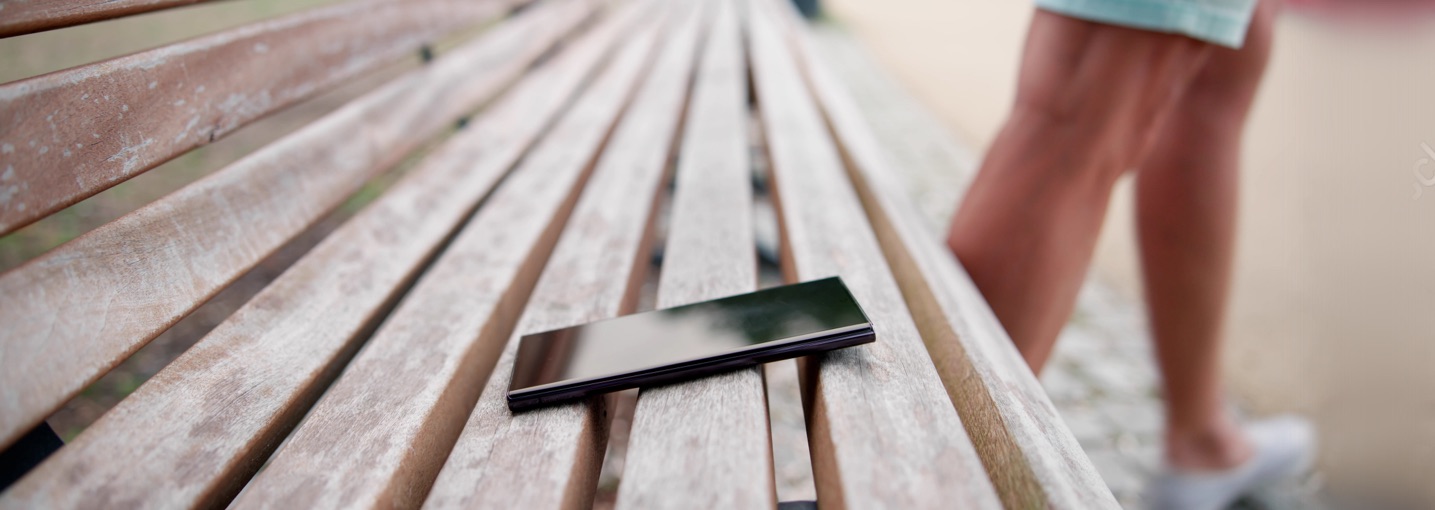 Smartphone dimenticato su una panchina del parco mentre una persona si allontana, a rischio furto.