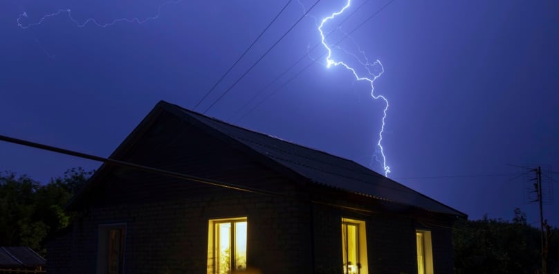 Fulmine colpisce vicino a una casa isolata di notte, un esempio degli eventi naturali estremi per cui assicurarsi.