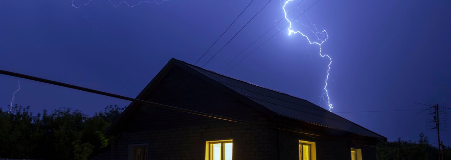 Fulmine colpisce vicino a una casa isolata di notte, un esempio degli eventi naturali estremi per cui assicurarsi.