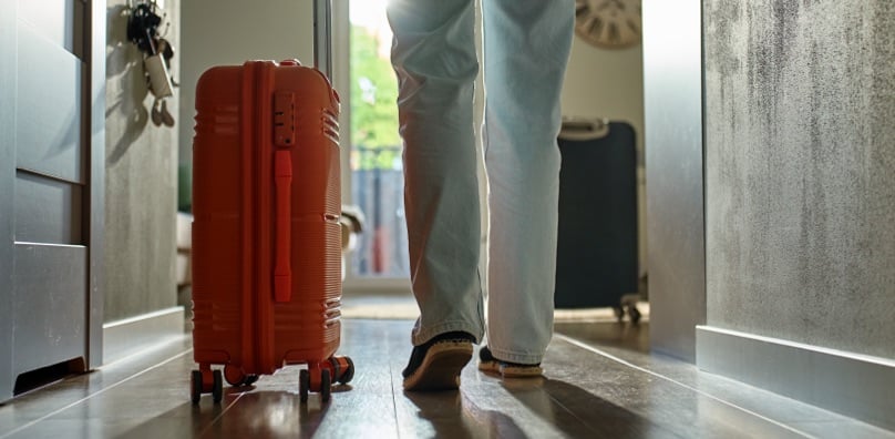 Persona esce di casa con una valigia prima di un viaggio, situazione a rischio per i furti in vacanza.