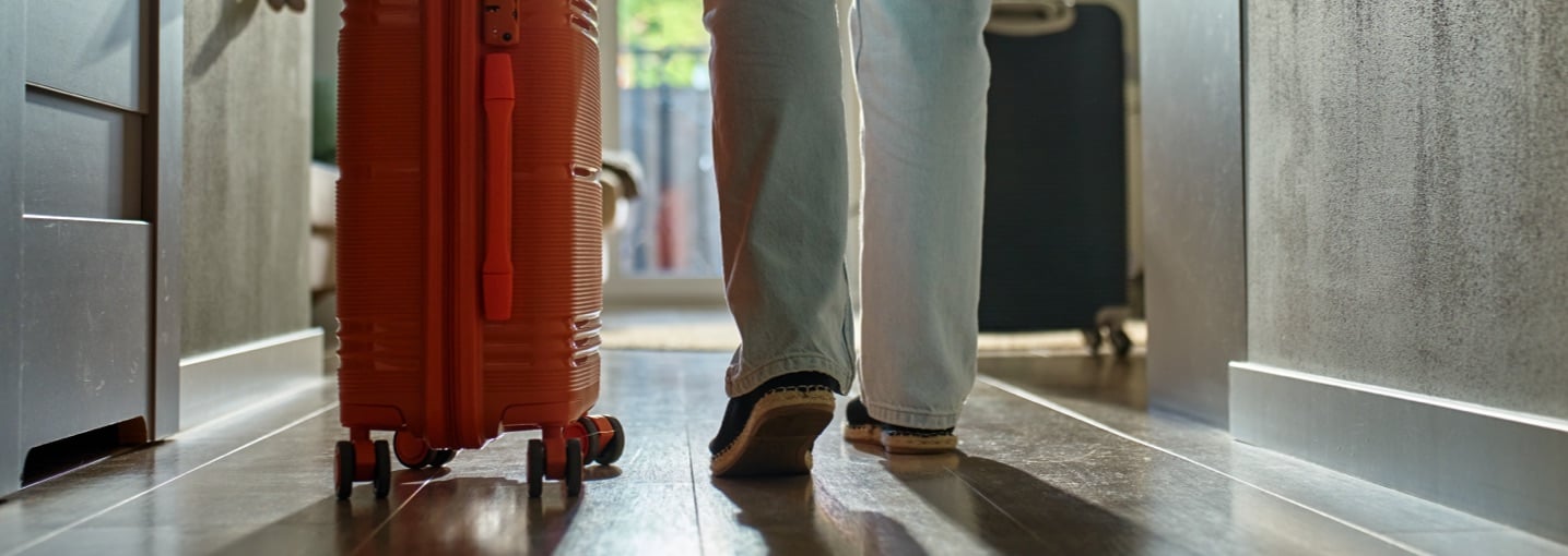 Persona esce di casa con una valigia prima di un viaggio, situazione a rischio per i furti in vacanza.