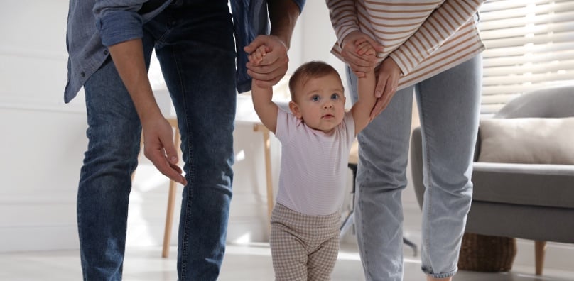 Coppia di genitori conviventi sostiene per mano il bambino piccolo mentre impara a camminare