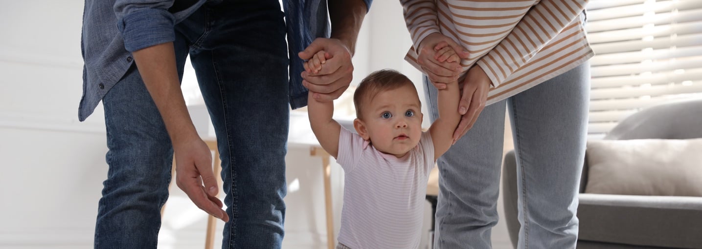 Coppia di genitori conviventi sostiene per mano il bambino piccolo mentre impara a camminare