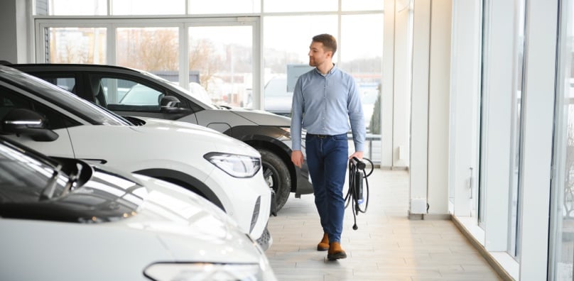 Un uomo cammina in un concessionario con un cavo di ricarica per valutare la convenienza delle auto ibride plug-in.
