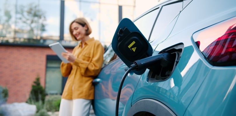 Auto in carica con donna che usa un tablet sullo sfondo per verificare le esenzioni del bollo auto elettriche.