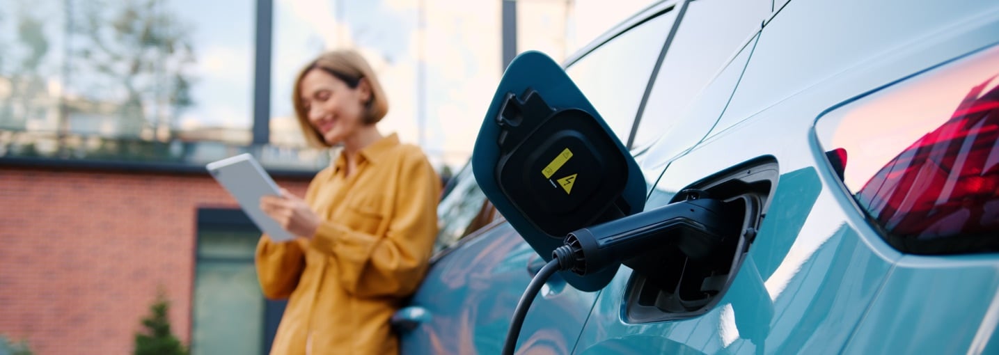 Auto in carica con donna che usa un tablet sullo sfondo per verificare le esenzioni del bollo auto elettriche.