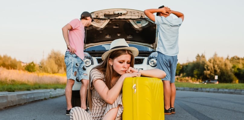 Ragazza triste su una valigia e auto in panne, metafora di un incidente all'estero che rovina la vacanza.