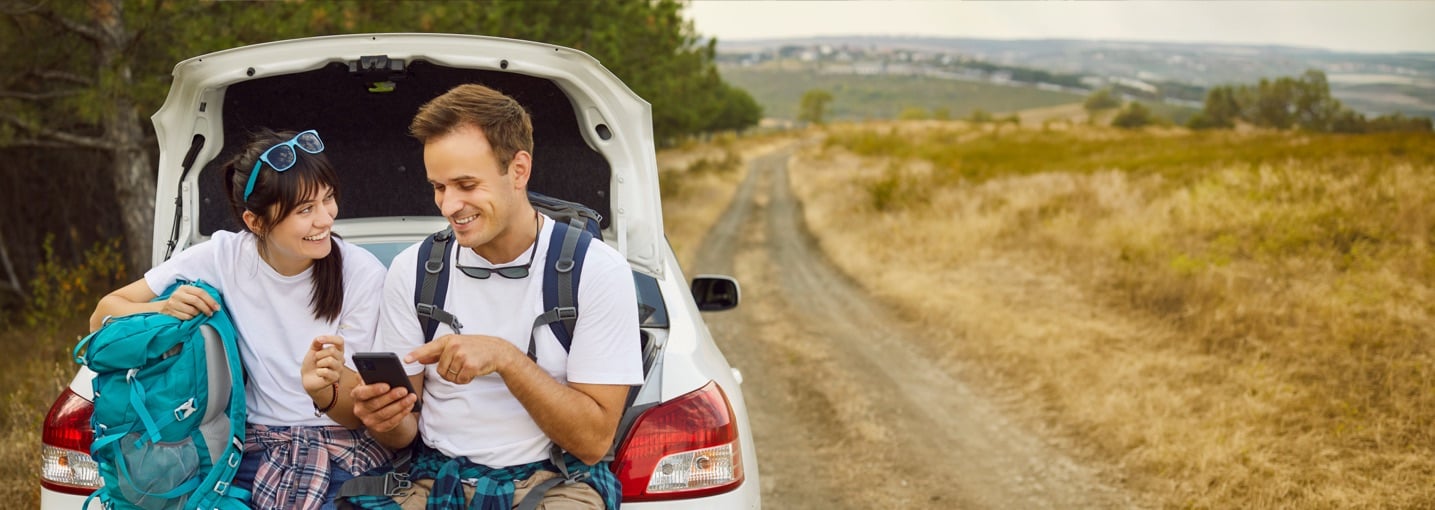 Giovani viaggiatori con zaini che guardano il telefono per risparmiare strada e tappe durante le vacanze in auto.