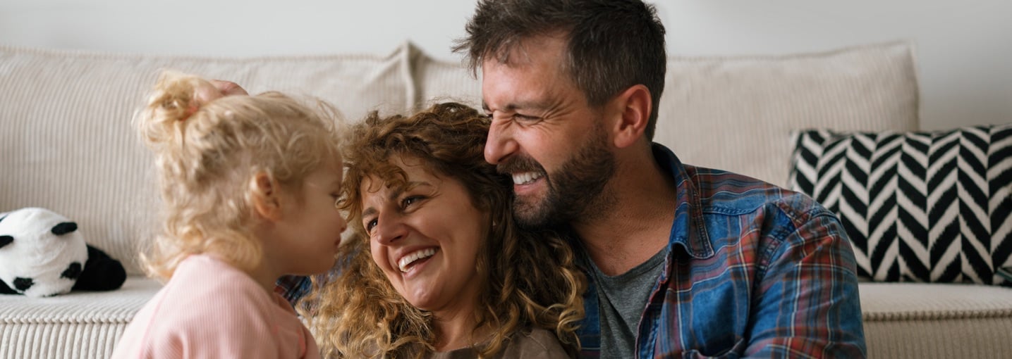 Famiglia felice in soggiorno che sorride, simbolo di serenità e assicurazioni per un futuro sicuro.