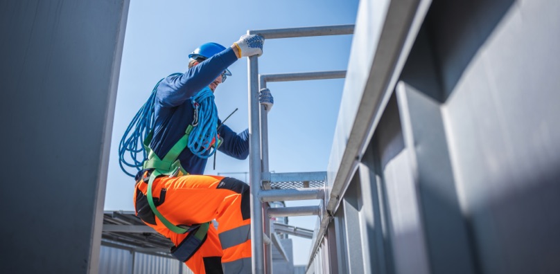Operaio con imbracatura di sicurezza ed elmetto che sale una scala in cantiere.